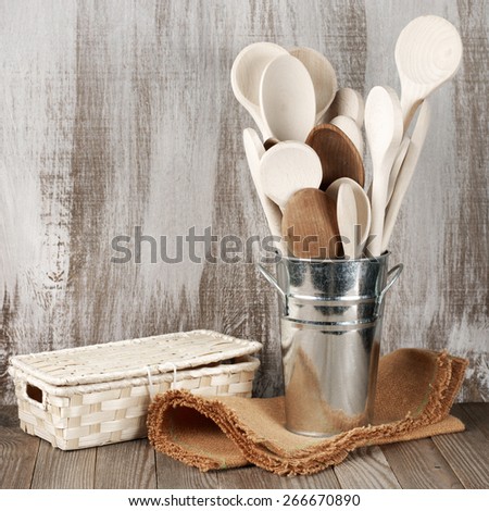 Assorted wood spoons in galvanized bucket and wicker box on rustic wooden background.