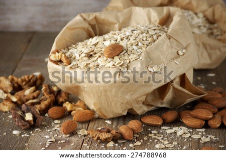 Dry oatmeal flakes with walnuts and almonds in paper bag on rustic wooden background.