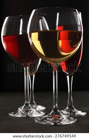 Various glasses of red and white wine with abstract pattern on black wooden background.