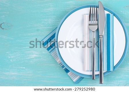 Table setting: white plate, fork and knife with napkins on aquamarine wooden table. Top view point.