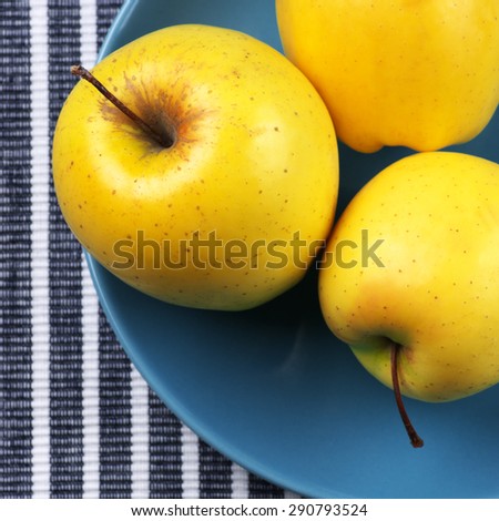 Yellow Golden Delicious apples in blue plate on striped tablecloth. Top view point.