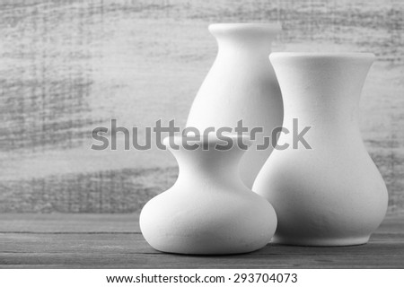 Three empty white unglazed ceramic vases on wooden table against rustic wooden wall. Black and white image. Shallow DOF, focus on front small vase.