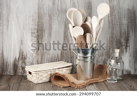 Wood spoons in galvanized bucket, wicker box and glass bottles on rustic wooden background.