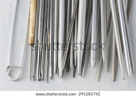 Set of vintage gray metallic knitting needles and crochets on rustic wooden table close-up. Shallow DOF.
