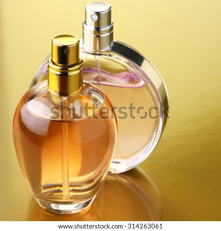 Two bottles of woman perfume on gold background.