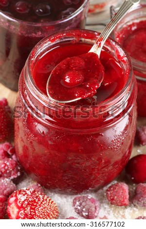 Assorted jams in glass jars and strawberry jam in spoon close-up. Shallow DOF, focus on berry in spoon.