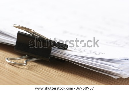 Pile of paper with metal clamp close-up. Selective focus on clamp and front edges of paper.