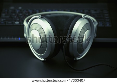 Metallic headphones and black keyboard on black background. Toned image.