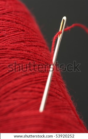 Close-up of needle with red thread in red reel on dark gray background.