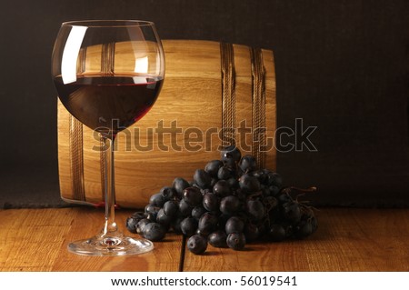 Glass of red wine, dark grape and souvenir barrel on wooden surface.