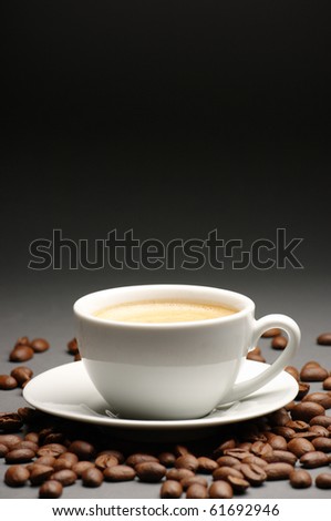 White cup of coffee with froth and coffee beans on dark gray background with copy space.
