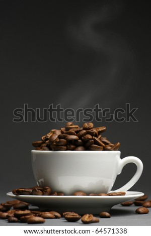 Hot roasted coffee beans in white cup with saucer on dark gray background.