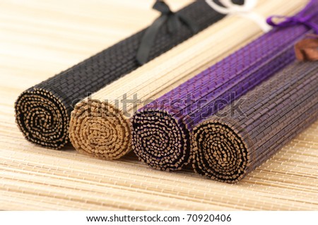Four multicolored rolled bamboo mats on mat surface.