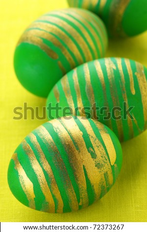 Close-up of green Easter eggs with gold ornament on yellow background.