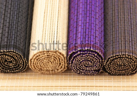 Close-up of four multicolored rolled bamboo mats on mat surface.