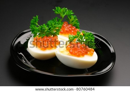 Canapes with egg, salmon caviar and parsley on black plate against dark background..