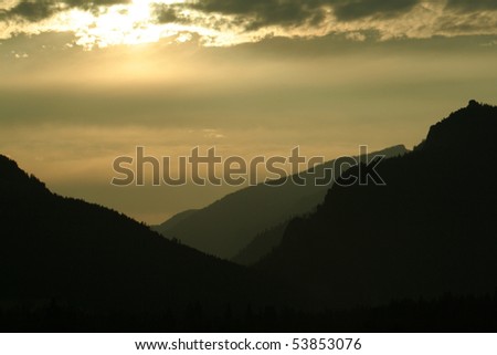 Gold sunset in clouds with silhouette of mountains.