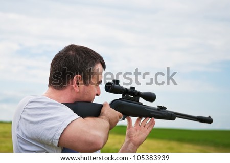 man aiming, looking into the scope of his rifle