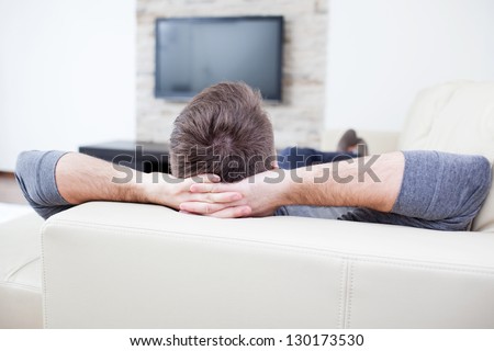 Relaxed man watching tv and lying on the couch.