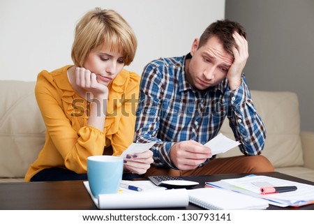 Sad, depressed young couple paying bills.