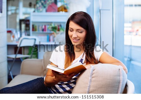 Happy woman reading book, sitting on couch