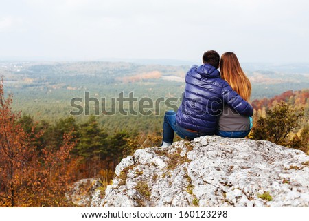 Couple in love sitting on mountain top watching autumn landscape