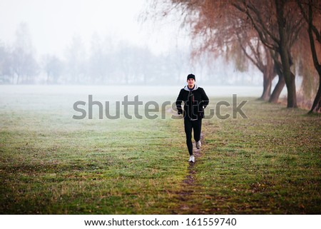 Man running during foggy weather at winter or autumn morning.
