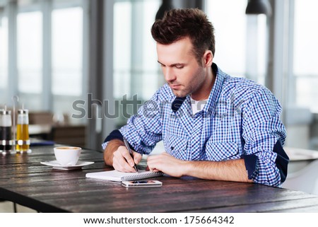 Young man sitting in a cafe and writing