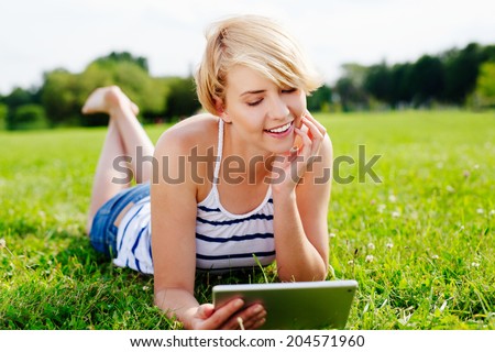 Photo of a pretty woman lying in the park and browsing the web on her tablet