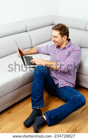 Young man sitting on the floor and browsing the web on a laptop