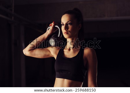 Attractive young woman holding kettlebell on her shoulder
