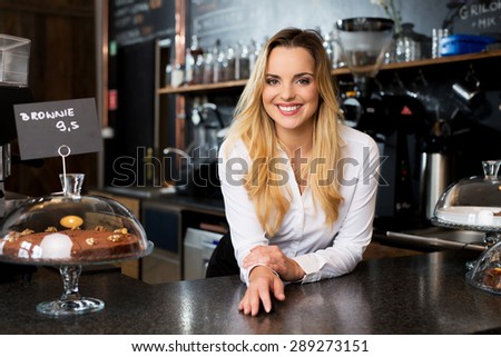 Smiling female cafe owner standing behind the bar