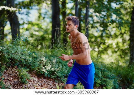 Young man running uphill in forest. Trial running.