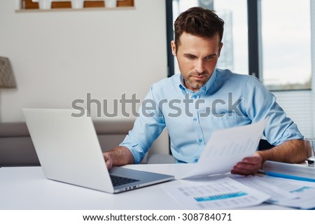 Young man working with laptop at home browsing bills and documents