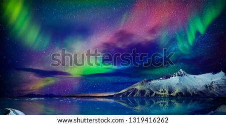  Gorgeous, unreal beautiful night view of the reflection of the northern lights in the water of the ocean and snow-capped mountains. Night Northern Lights is just an amazing sight.
