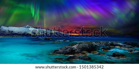  Gorgeous, unreal beautiful night view of the reflection of the northern lights in the water of the ocean and snow-capped mountains. Night Northern Lights is just an amazing sight.