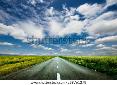 image of wide open prairie with a paved highway stretching out as far as the eye can see with beautiful small green hills under a bright blue sky in the summer time