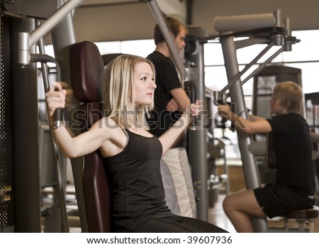 Girl using an exercise machine at a health club with two men in the background