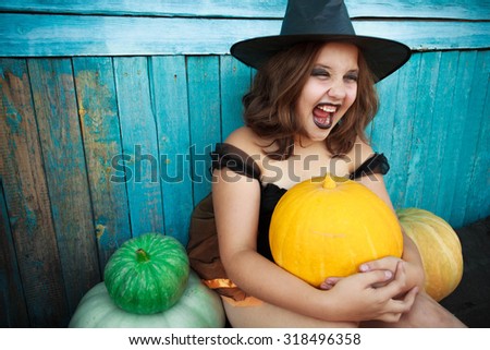 Halloween portrait of little girl in black hat and black clothing with pumpkin