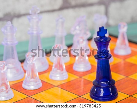 A blue king on the chess board confronting with a number of transparent glass chess pieces. - Business competition and leadership concept.