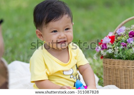 baby boy in yellow shirt sit and play toy with basket of flower in the park