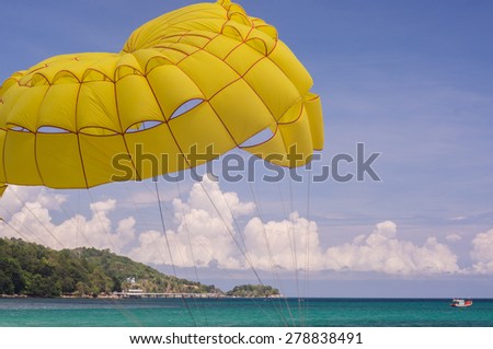 Bright yellow parachute carries it\'s riders from the sandy beach over the blue waters of the Andaman Sea
