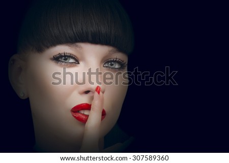 Beautiful woman making a silence gesture studio portrait dark background