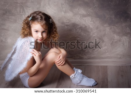 Studio shot of little girl as an angel seated on the floor
