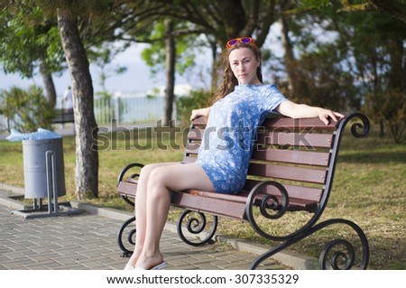Young long-haired woman in a blue dress sitting on a bench in the city of Anapa on a sunny summer evening
