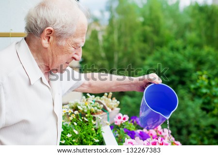 serious senior man watering the flowers on his balcony