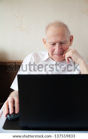 smiling old man holding computer mouse - he is working on a laptop