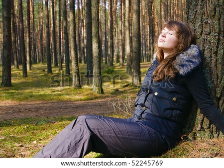 young beautiful girl sitting under the tree in the forest with her eyes closed, she is dreaming