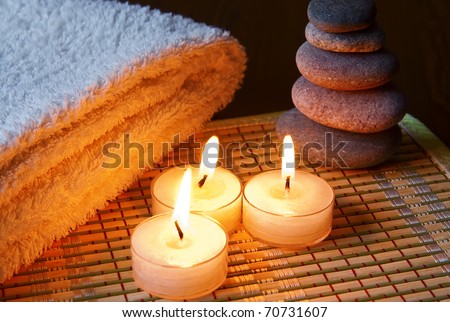 close-up three burning candles, gray stones and cotton towel on a bamboo napkin