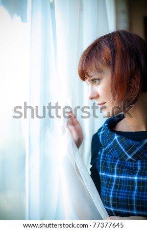 young woman looking through the window, she is waiting for somebody or something, or maybe watching someone